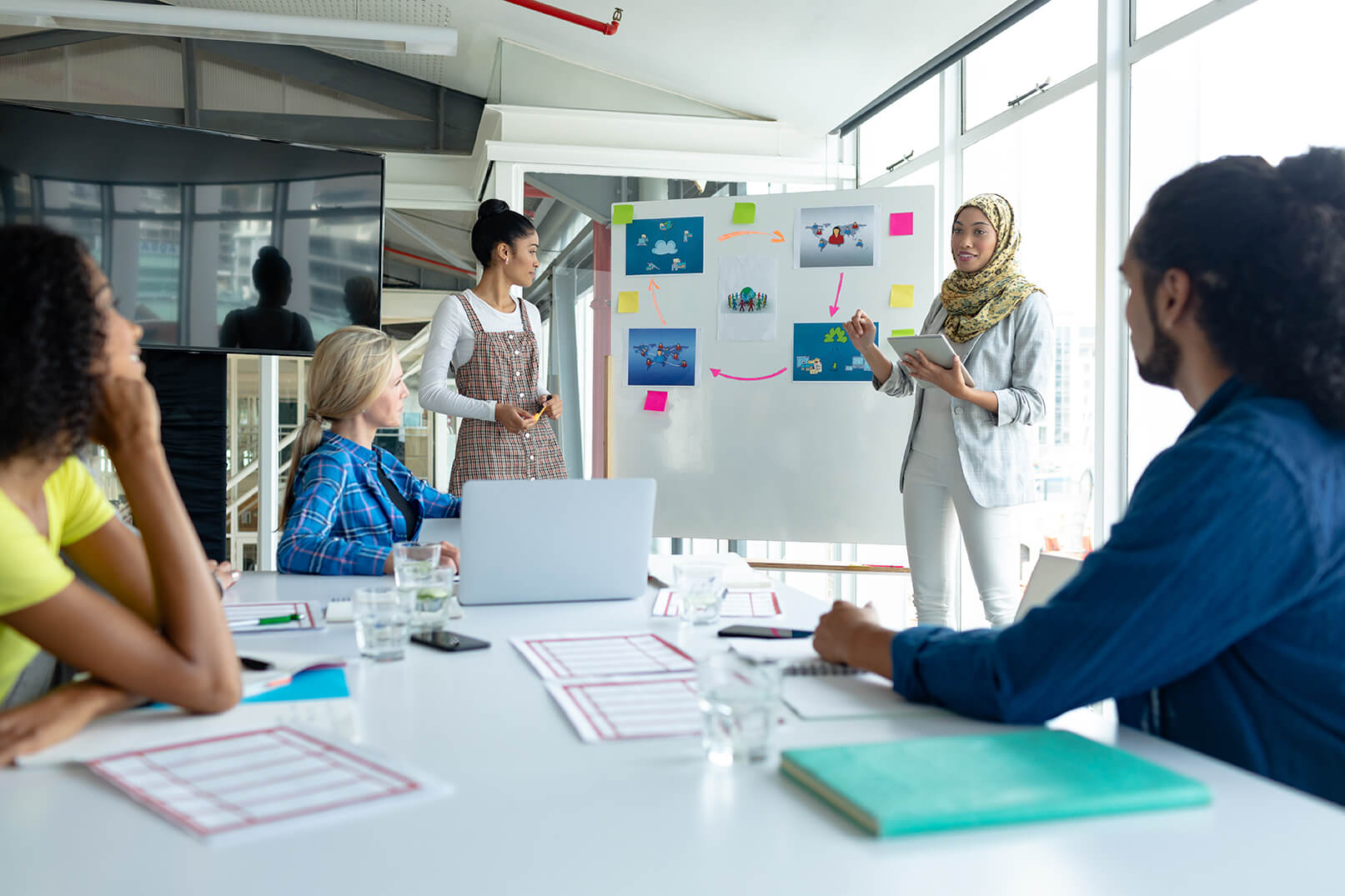 Front view of Mixed-race businesswoman in hijab giving presentation on flip chart during meeting in a modern office